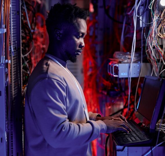 Side view portrait of black man as network administrator setting up servers and using laptop in neon light