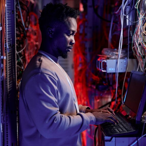 Side view portrait of black man as network administrator setting up servers and using laptop in neon light