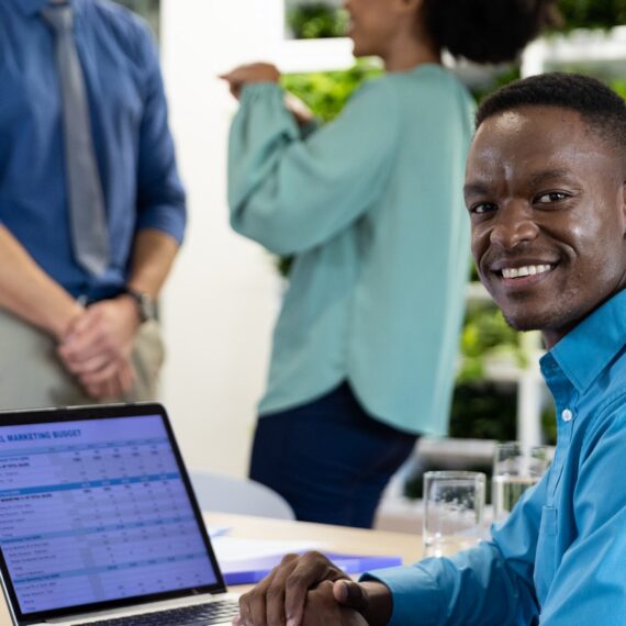 Portrait of happy african american businessman with laptop and diverse colleagues in modern office. Global business, finances and office concept.