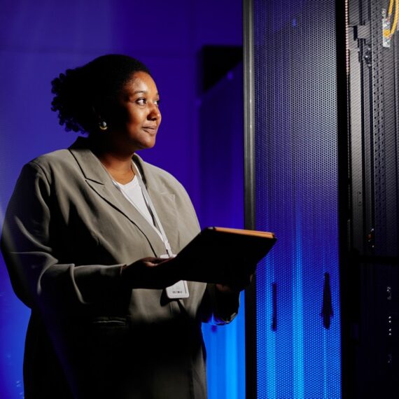 Waist up portrait of female system admin using tablet in server room lit by neon light, copy space